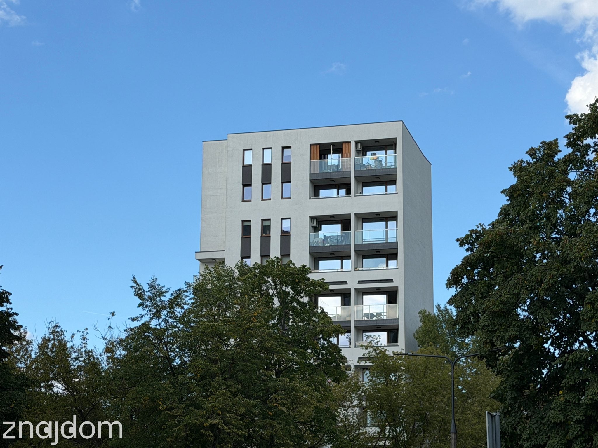 Widok na szczyt nowoczesnego apartamentowca ponad drzewami - Warszawa, Bielany.