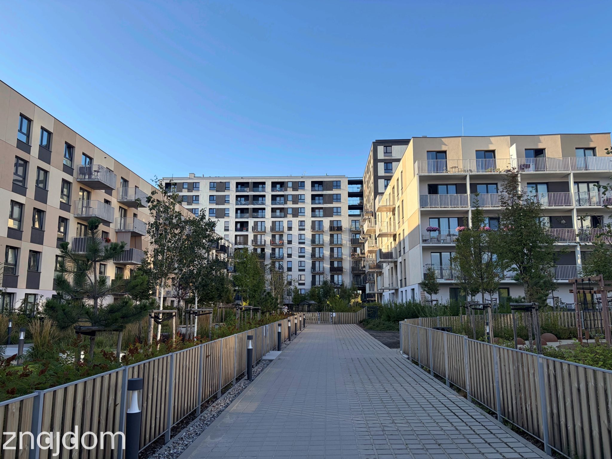 Nowe osiedle na Widzewie. Apartamentowce i chodnik oświetlony niskimi lampkami.