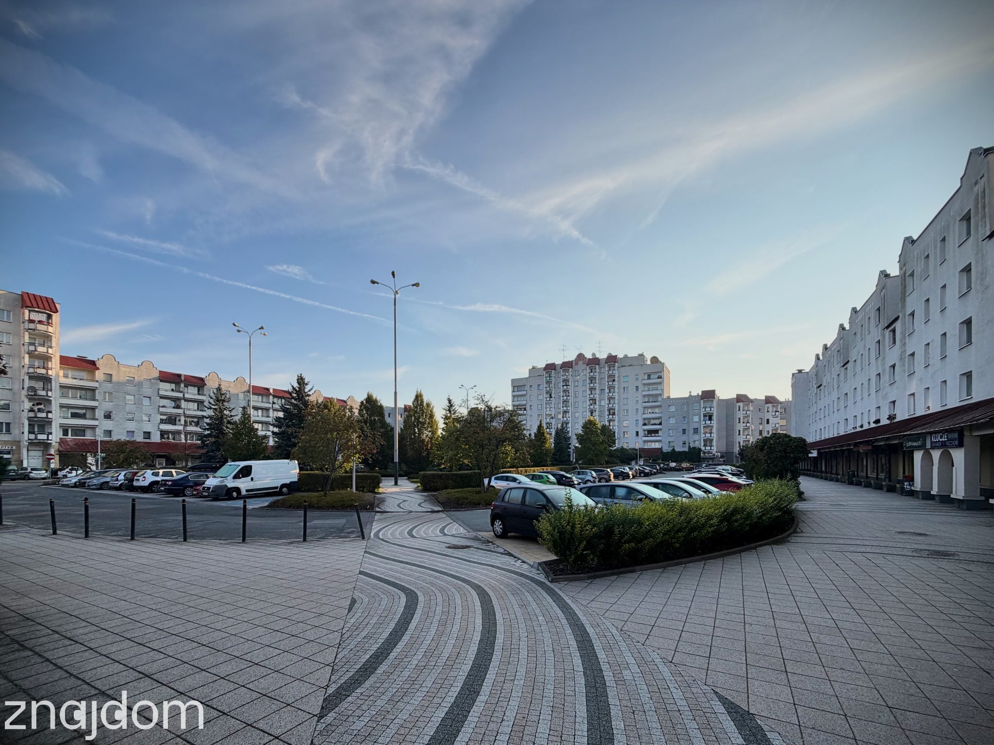 Zdjęcie samochodów zaparkowanych wokół skweru na Placu Słonecznym na Radogoszczu. Dookoła postmodernistyczne bloki z lat 90.