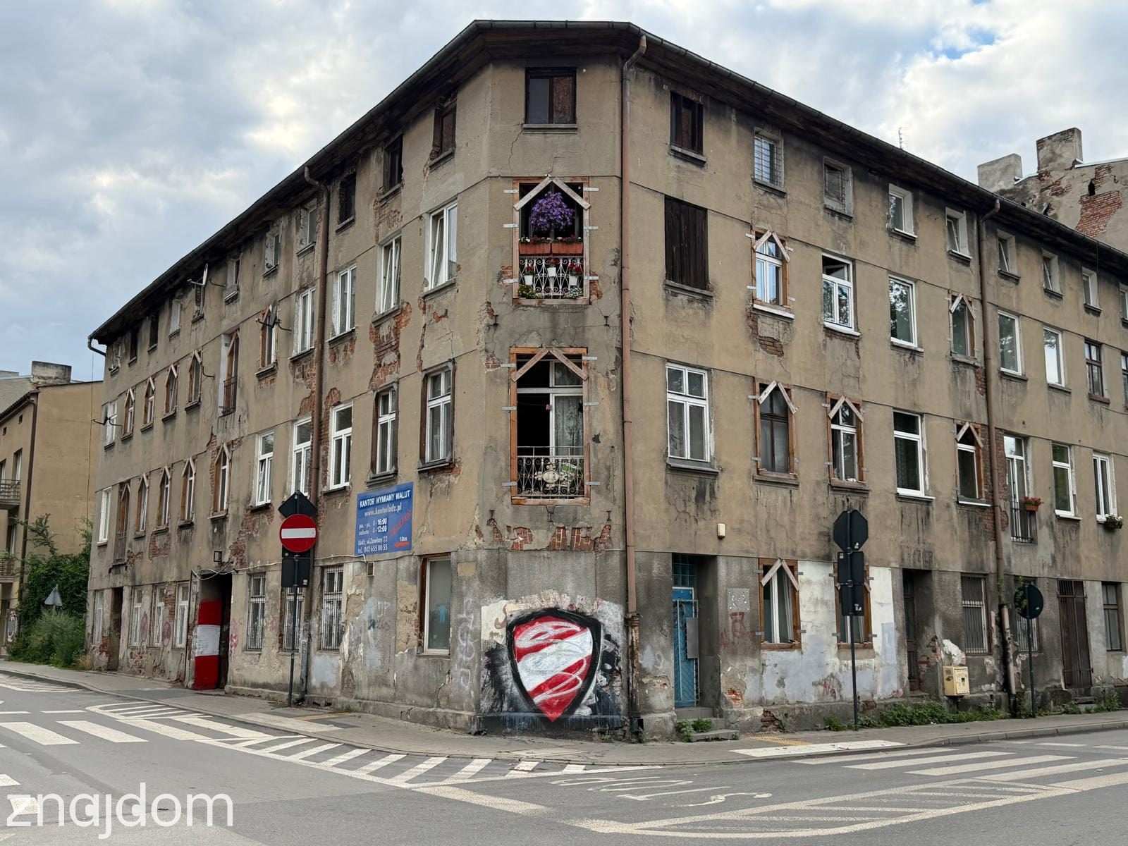 Zdjęcie przedstawia róg kamienicy na Bałutach. Graffiti i ozdobione okna na rogu.