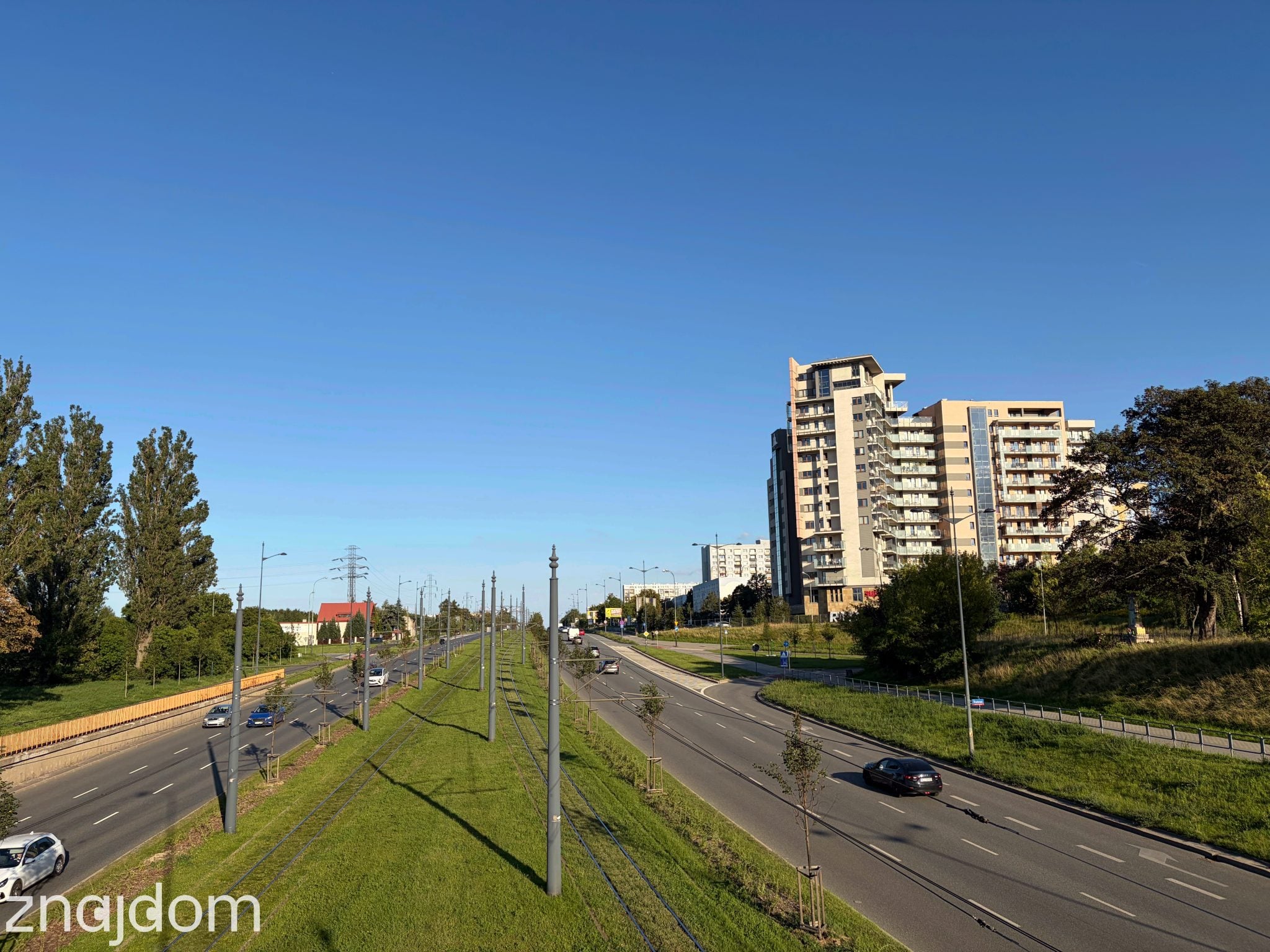 Panorama z kładki na ul. Piłsudskiego. Widok na dwie drogi jednokierunkowe oddzielone zielonym torowiskiem tramwajowym. Po lewej apartamentowiec Panoramika.