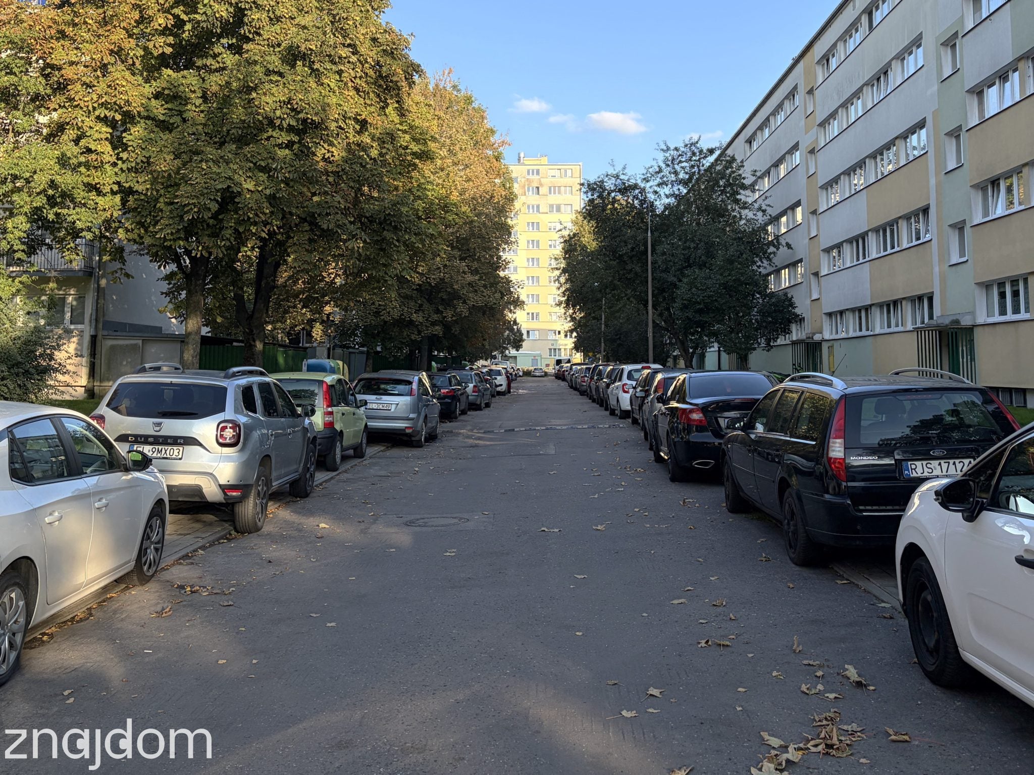 Wąska osiedlowa uliczka zastawiona zaparkowanymi samochodami między blokami na łódzkim Teofilowie