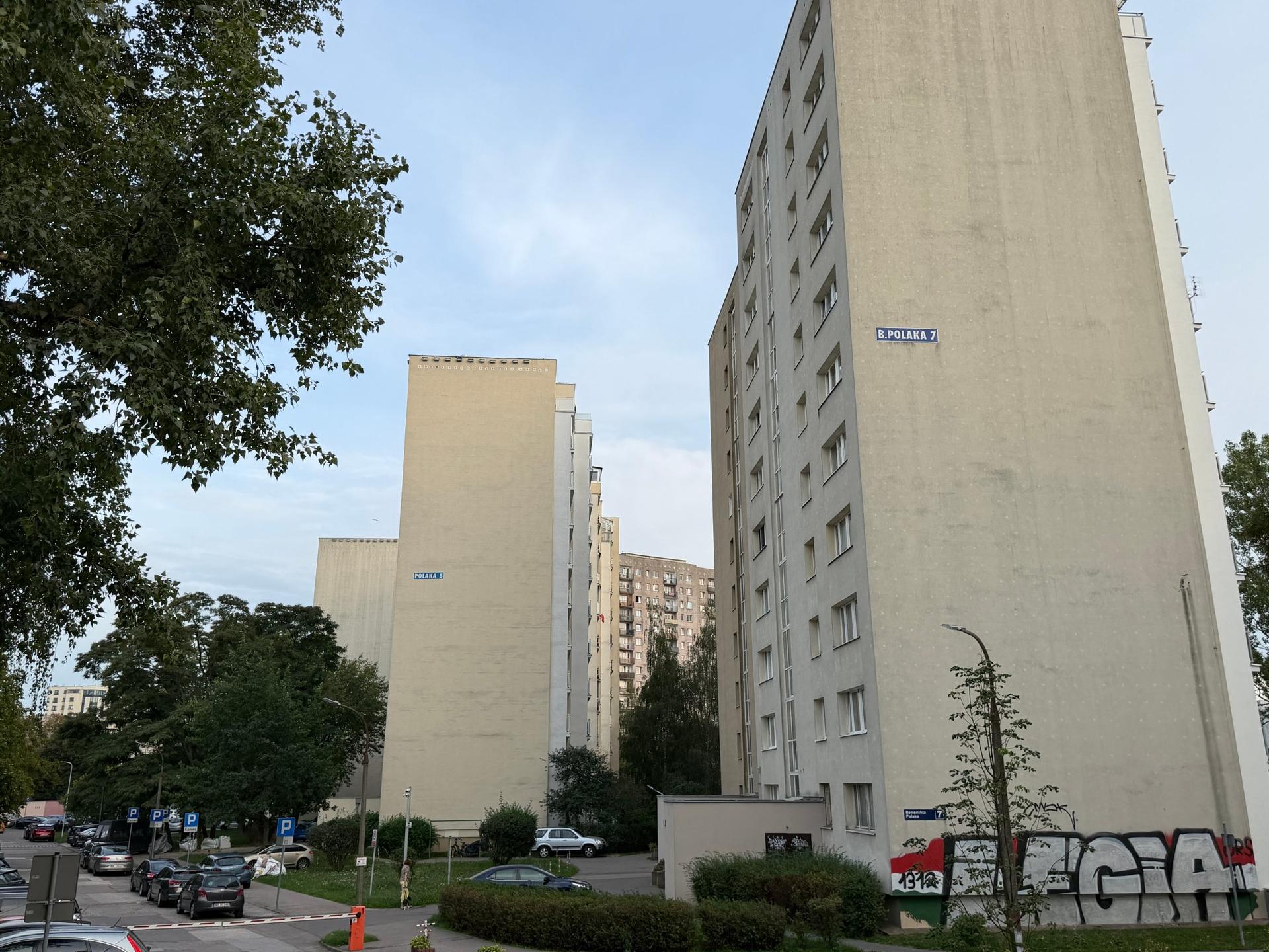 Wysokie, modernistyczne bloki z wielkiej płyty otoczone dojrzałą zielenią na warszawskim Ursynowie.