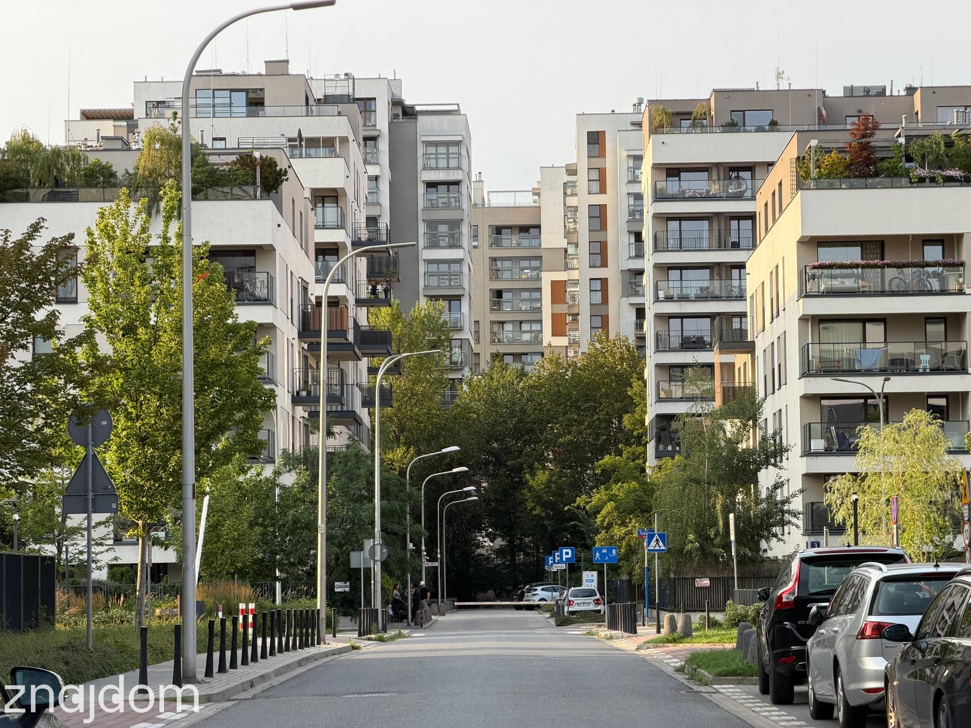 Nowoczesne, gęste osiedle apartamentowców z jasnymi elewacjami, balkonami i dużą ilością zieleni na warszawskim Mokotowie.