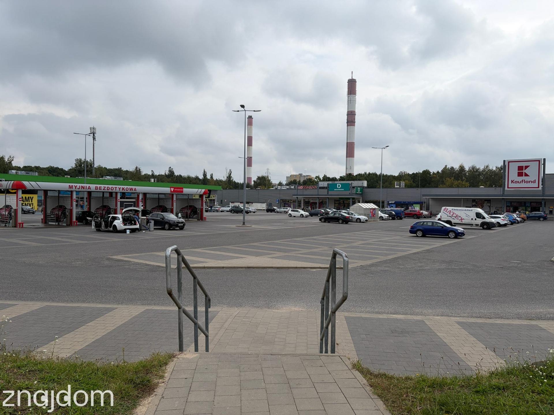 Widok ze schodków na parking centrum handlowego przy Rondzie Sybiraków. Na parkingu myjnia.