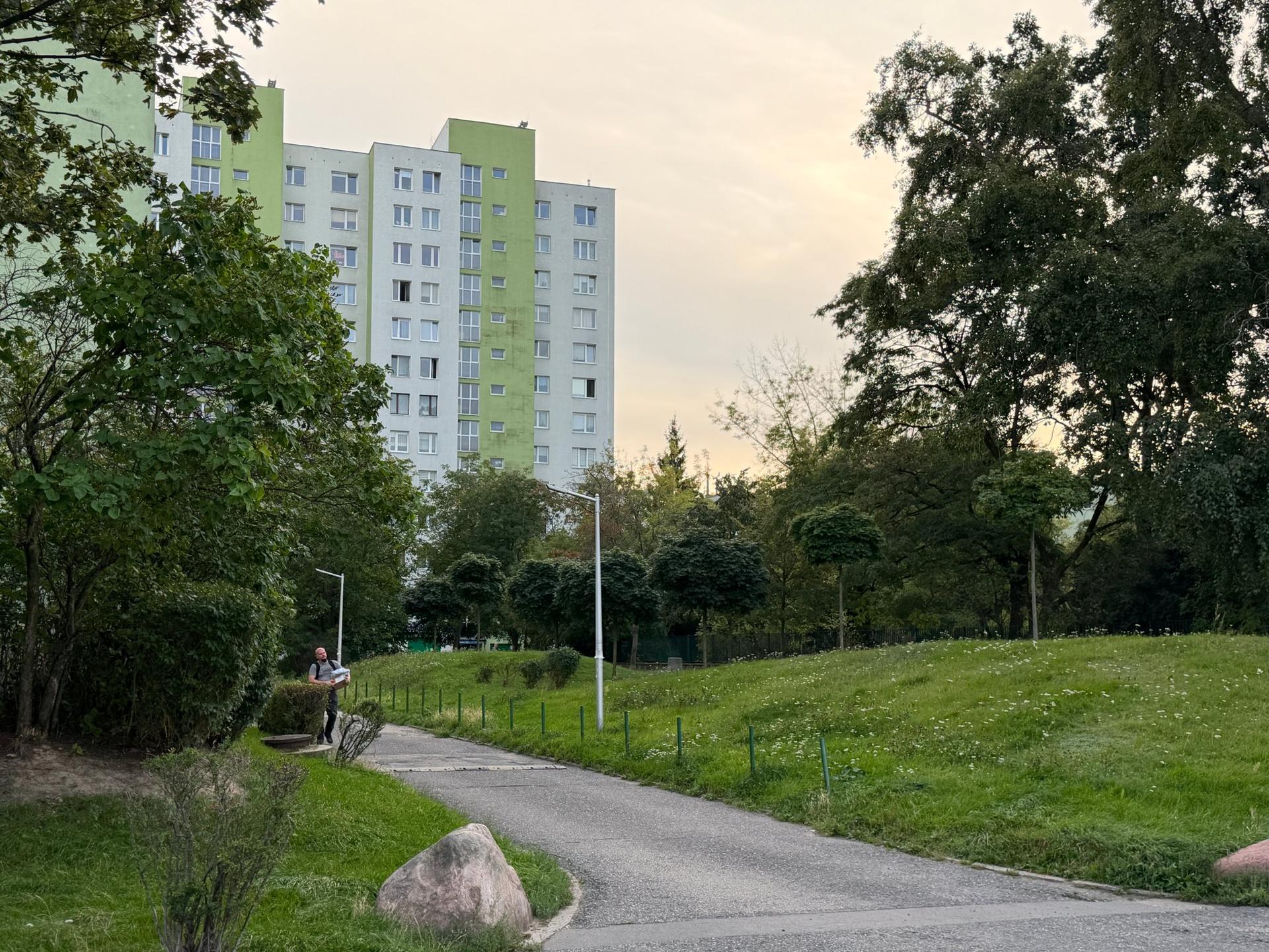 Wysoki blok mieszkalny otoczony rozległymi terenami zielonymi i alejką spacerową na warszawskim Ursynowie.