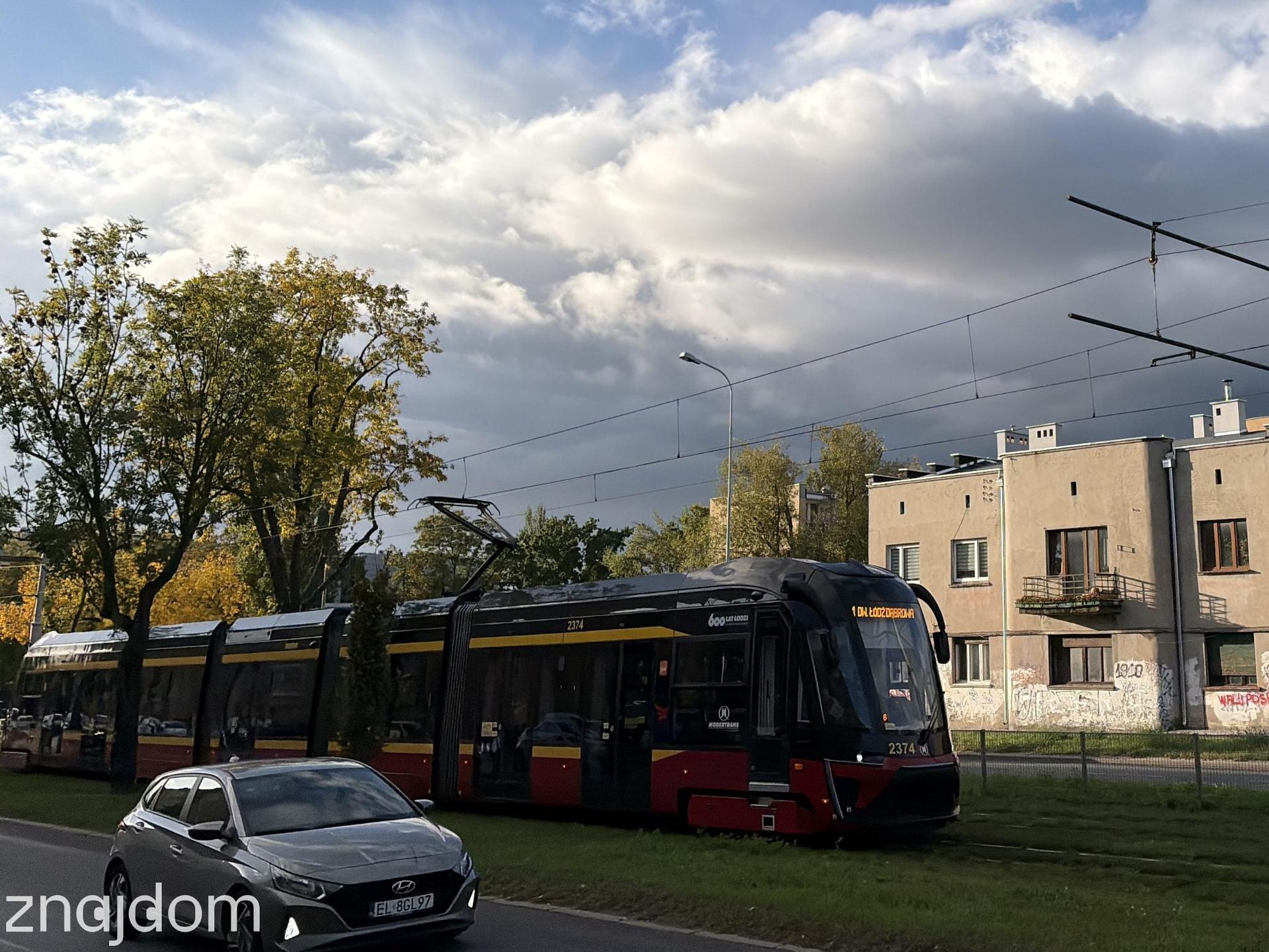 Nowoczesny tramwaj miejski z napisem Dąbrowa na wyświetlaczu jadący wzdłuż dwupasmowej jezdni.