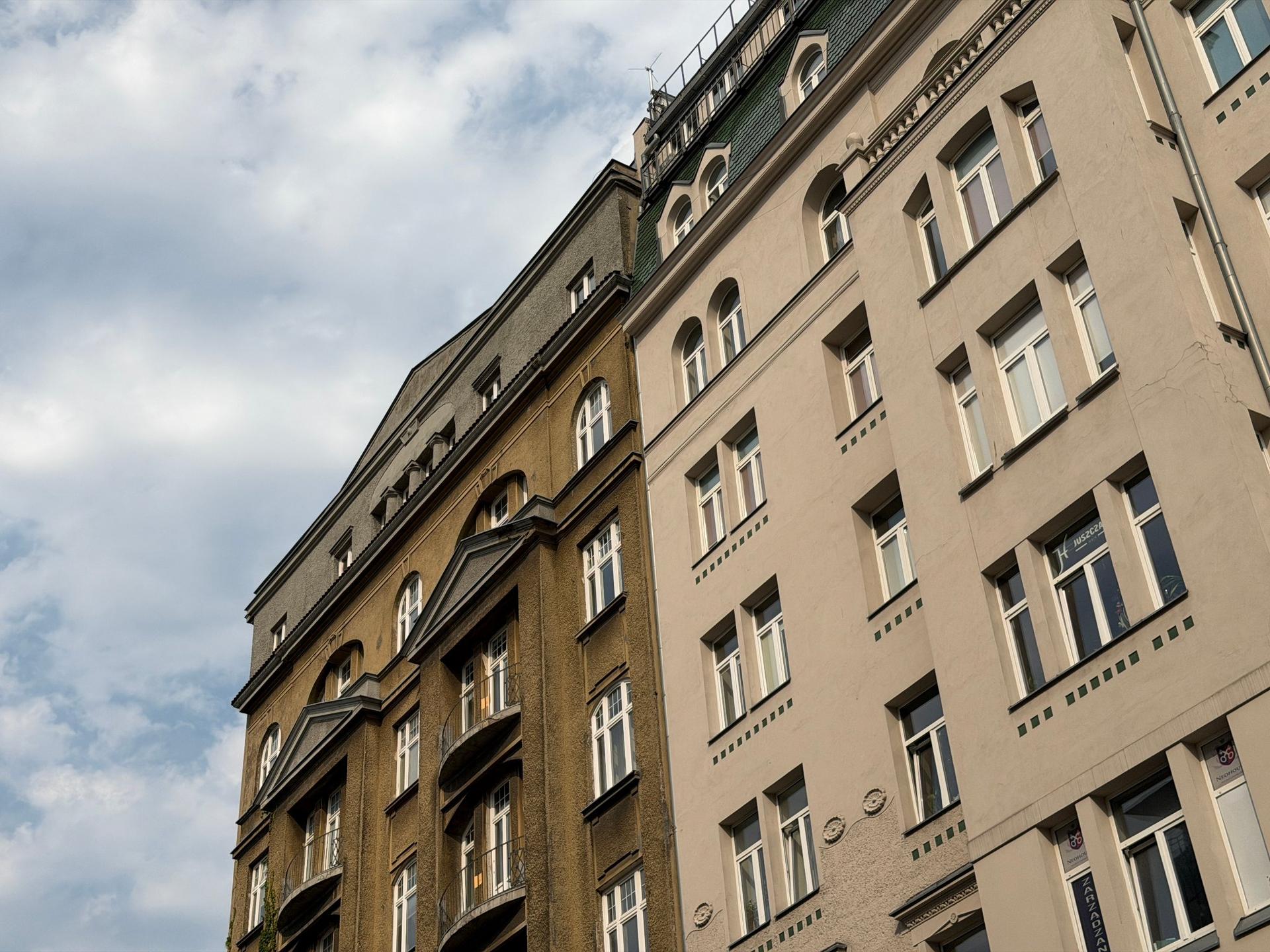 Zabytkowe, wysokie kamienice ze zdobionymi fasadami, ujęte z żabiej perspektywy na warszawskim Śródmieściu.
