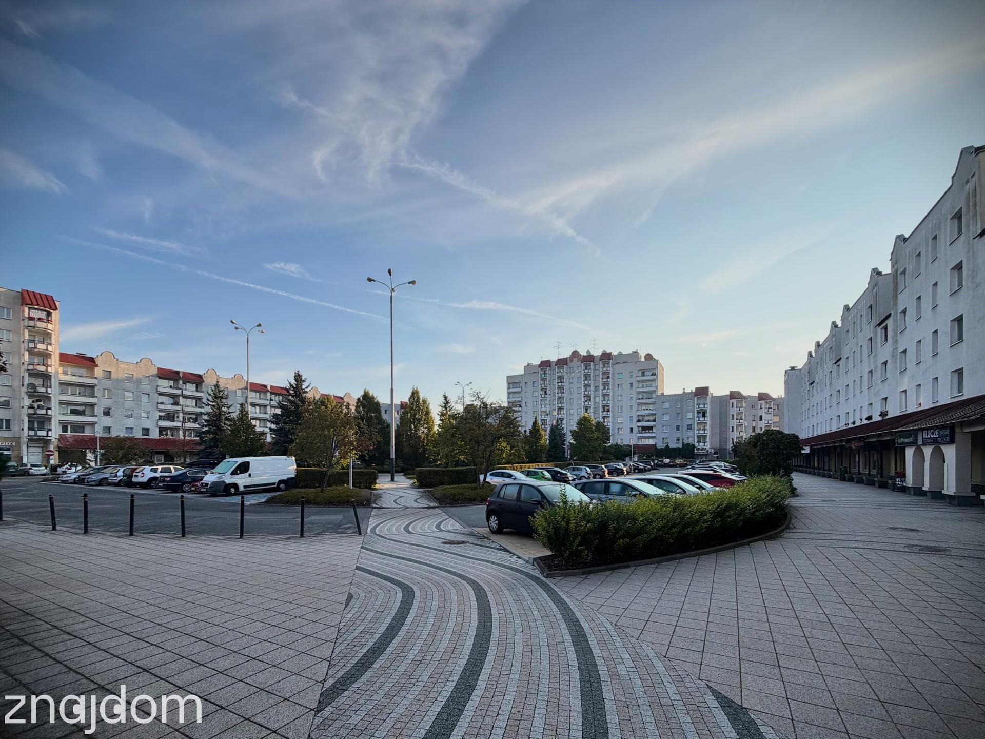 Zdjęcie samochodów zaparkowanych wokół skweru na Placu Słonecznym na Radogoszczu. Dookoła postmodernistyczne bloki z lat 90.