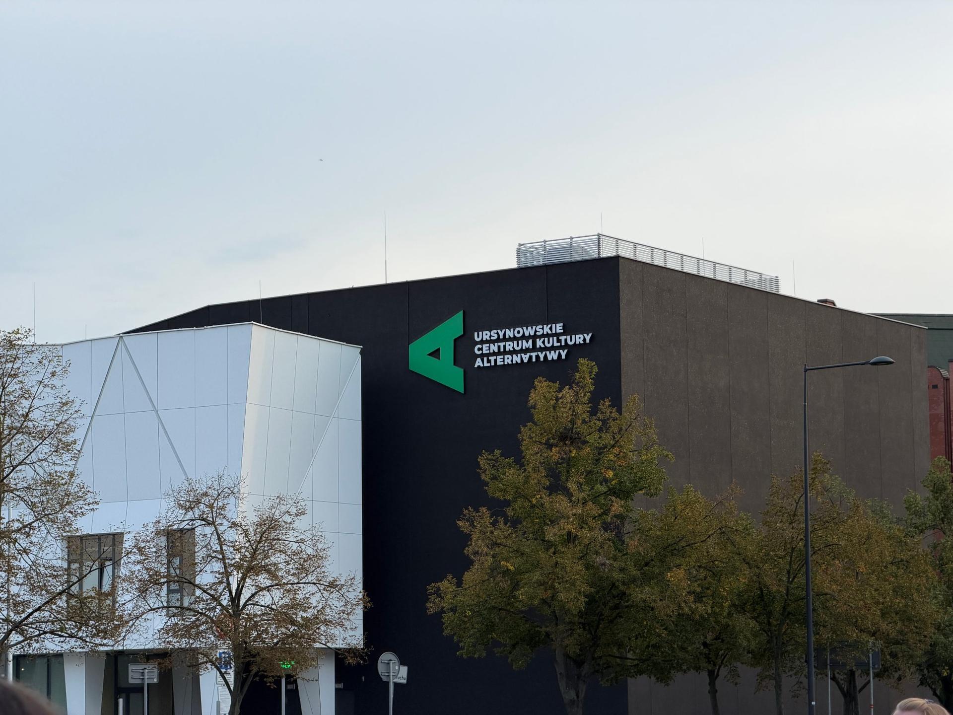 Nowoczesna, geometryczna bryła budynku Ursynowskiego Centrum Kultury „Alternatywy” w otoczeniu zieleni na warszawskim Ursynowie.