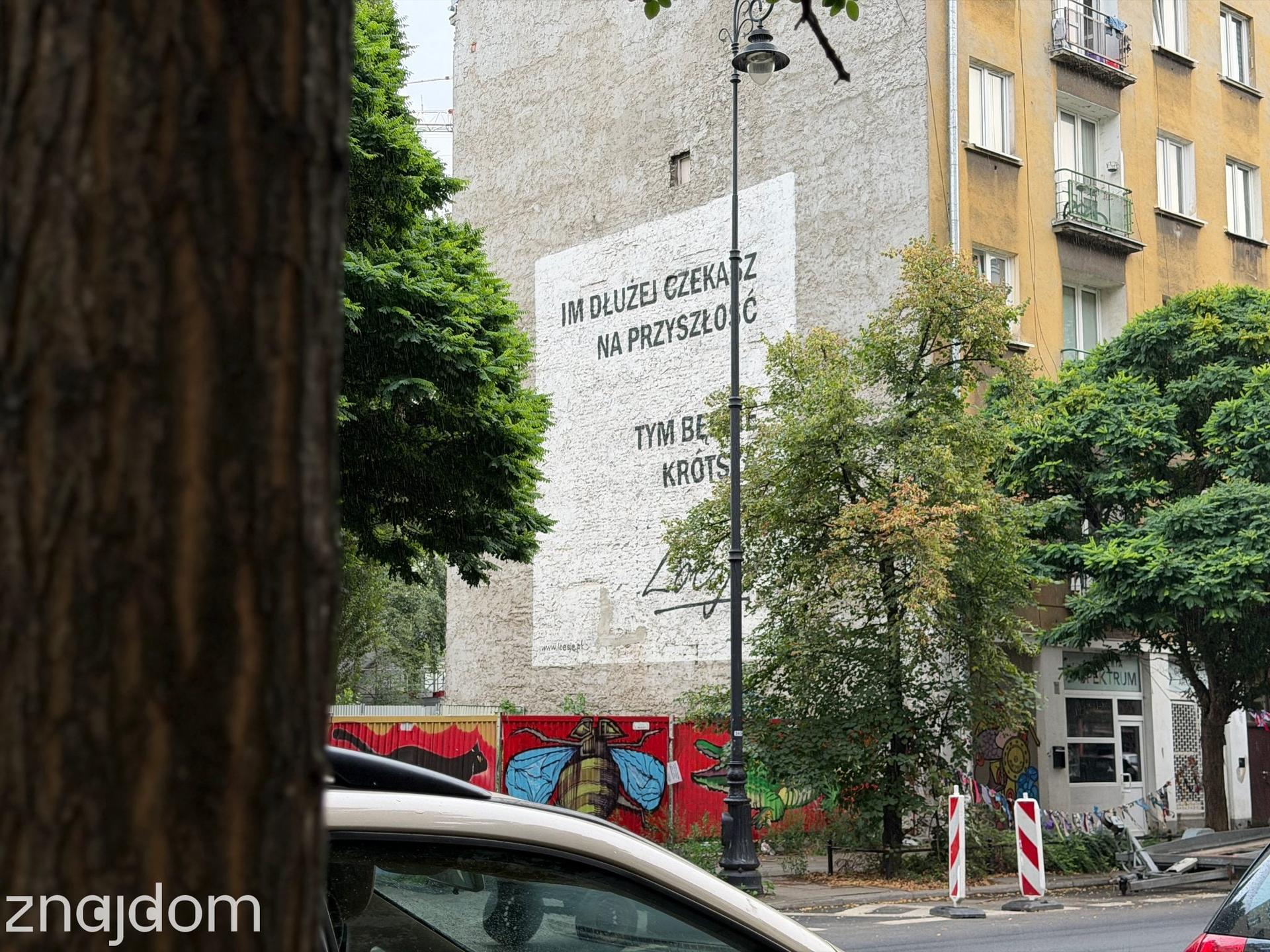 Ściana praskiej kamienicy z czarno-białym muralem tekstowym grupy Loesje oraz kolorowym graffiti na dolnym ogrodzeniu.
