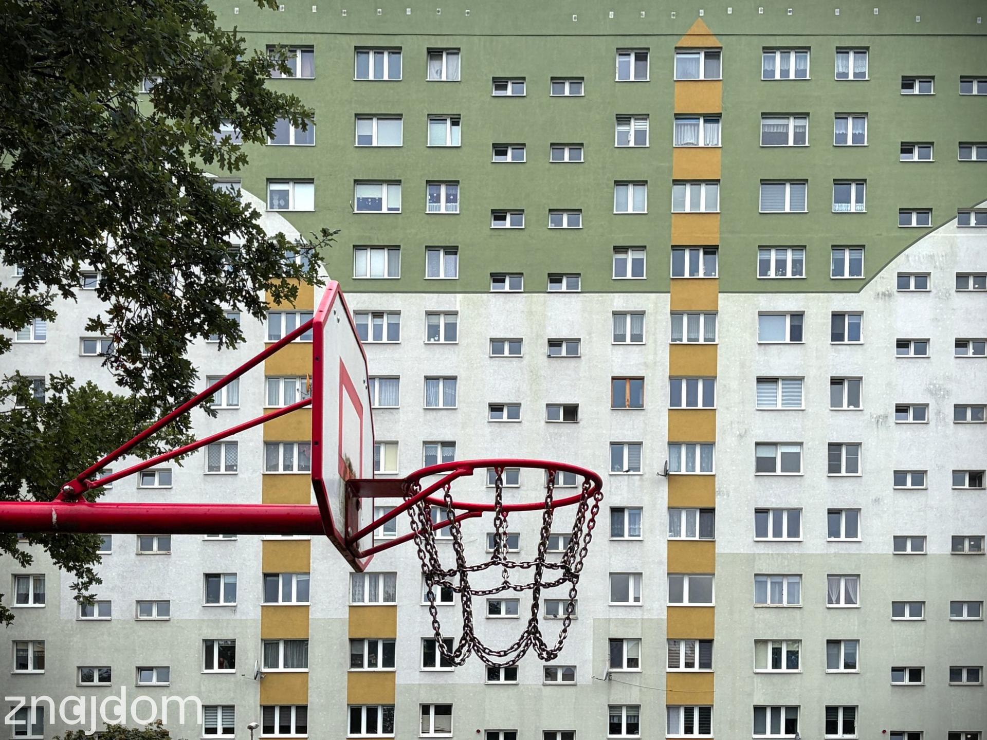 Zbliżenie na kosz do gry w koszykówkę na tle szerokiego bloku na Widzewie Wschód.