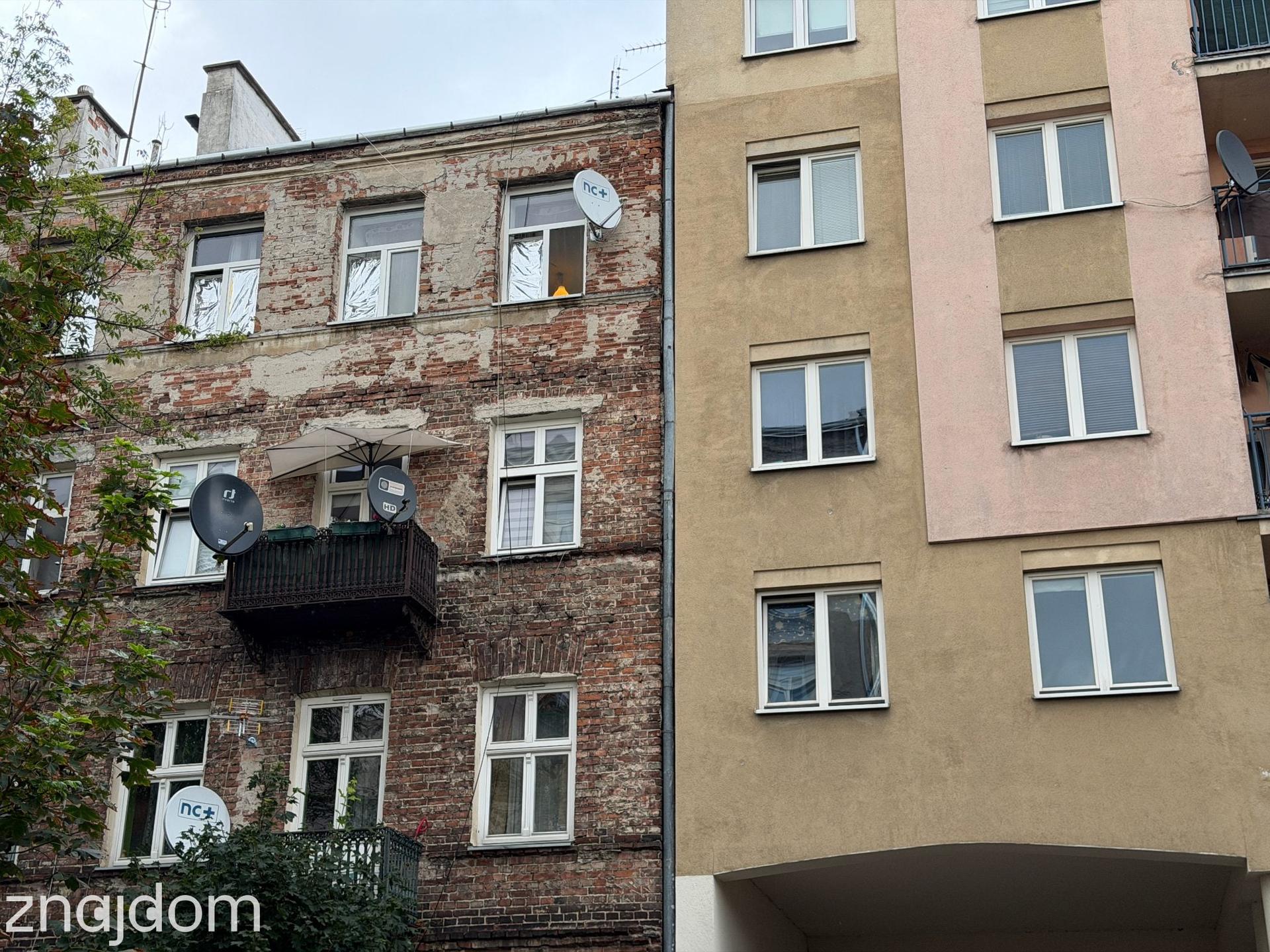 Surowa, ceglana kamienica przylegająca do nowszego budynku mieszkalnego na Pradze-Północ.