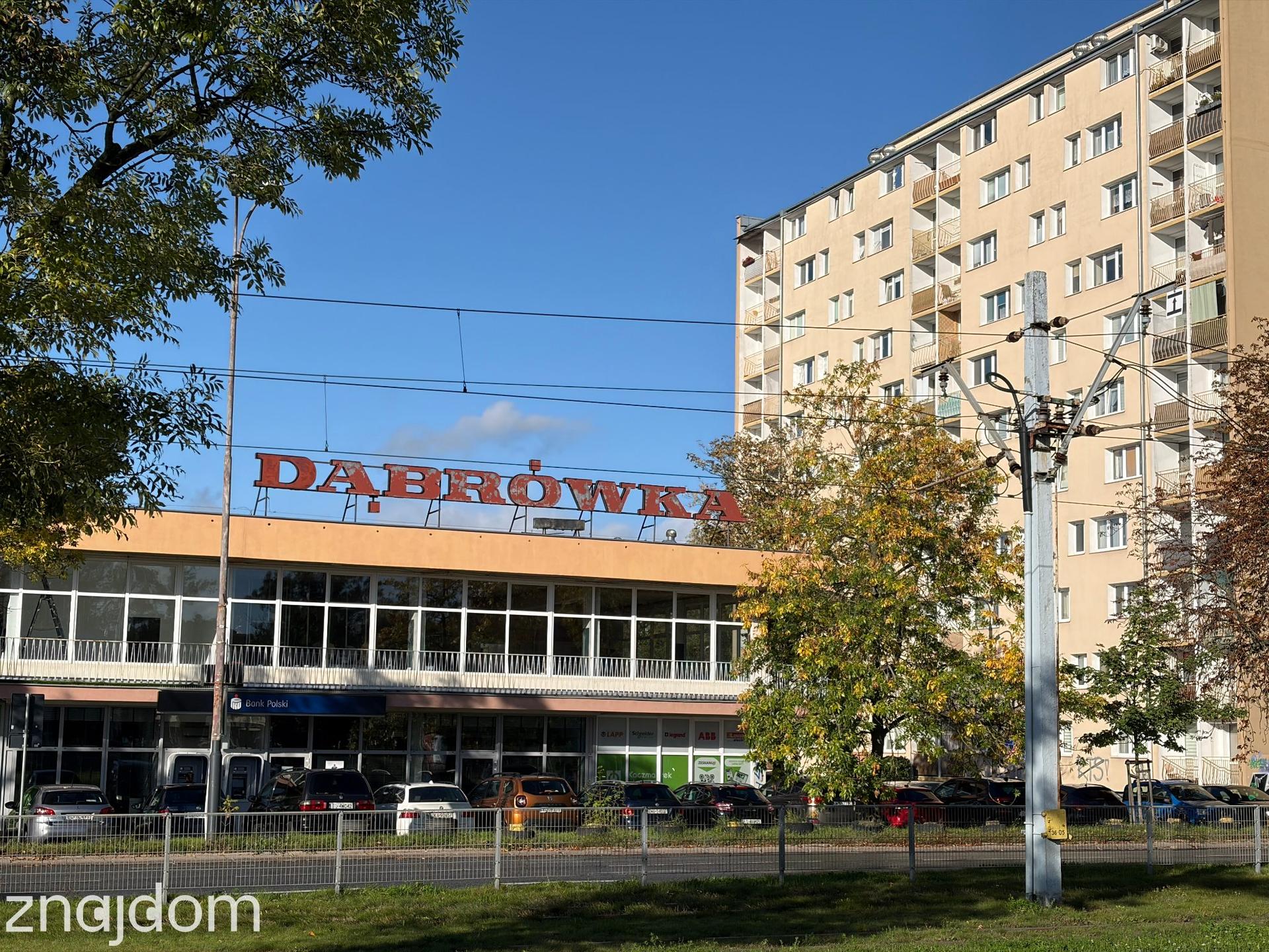 Pawilon handlowy z neonem Dąbrówka na tle bloku z wielkiej płyty na osiedlu Łódź Dąbrowa.
