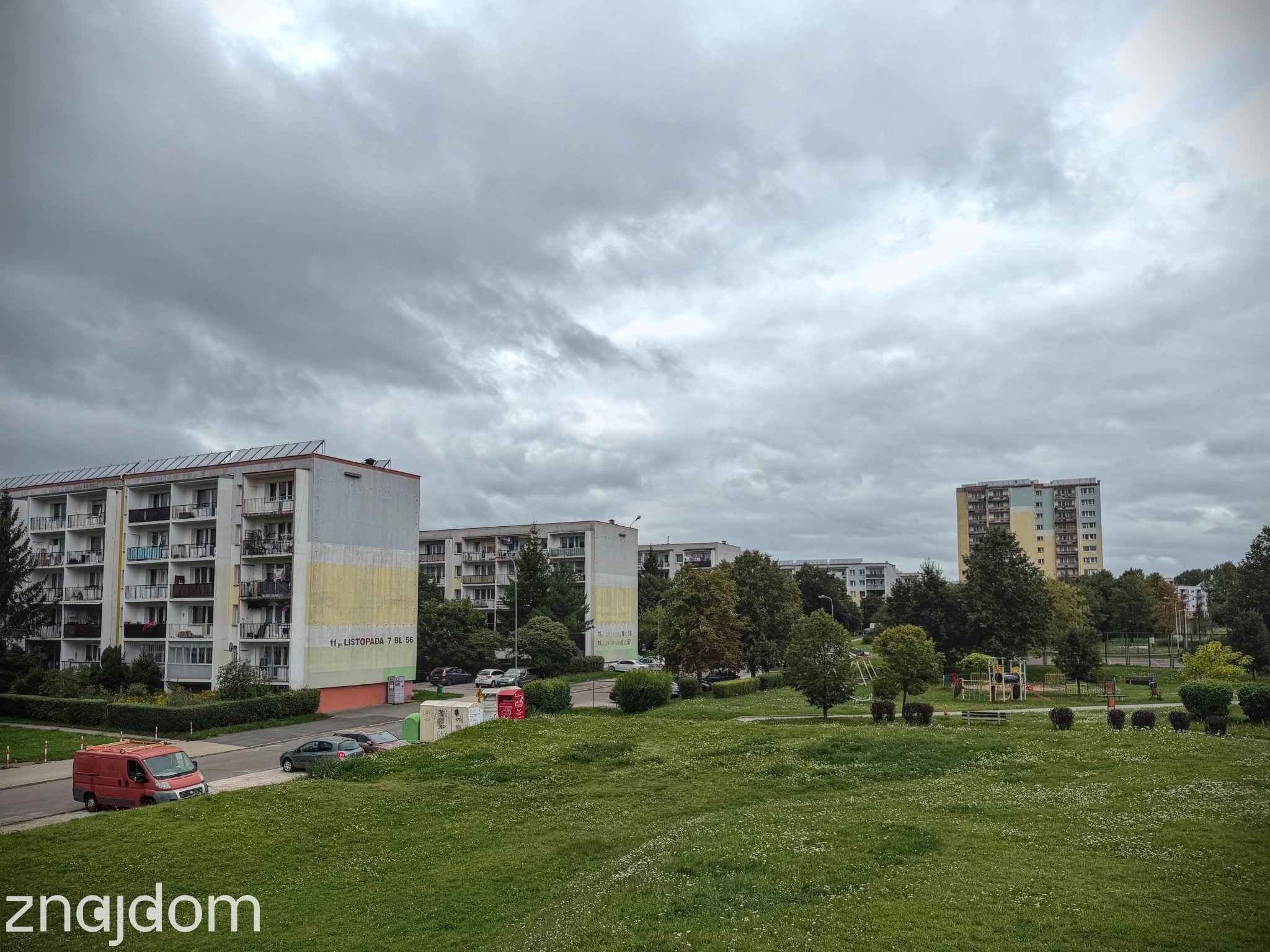 Widok z zielonej górki na bloki na Radogoszczu Zachód. Dookoła drzewa i plac zabaw.